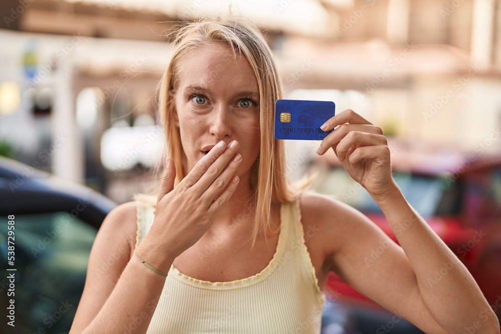 Sticker Young caucasian woman holding credit card covering mouth with hand, shocked and afraid for mistake. surprised expression