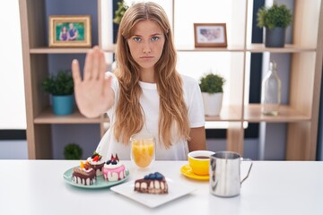 Obraz na płótnie Canvas Young caucasian woman eating pastries t for breakfast doing stop sing with palm of the hand. warning expression with negative and serious gesture on the face.