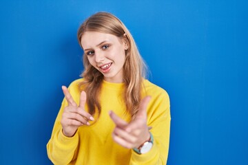 Young caucasian woman standing over blue background pointing fingers to camera with happy and funny face. good energy and vibes.