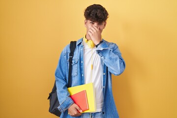 Hispanic teenager wearing student backpack and holding books smelling something stinky and...