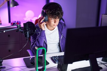 Young hispanic teenager streamer playing video game using computer at gaming room