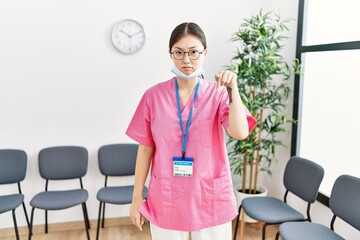 Fototapeta na wymiar Young asian nurse woman at medical waiting room pointing down looking sad and upset, indicating direction with fingers, unhappy and depressed.