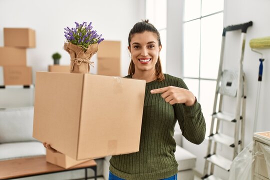 Young hispanic woman holding cardboard box at moving smiling happy pointing with hand and finger
