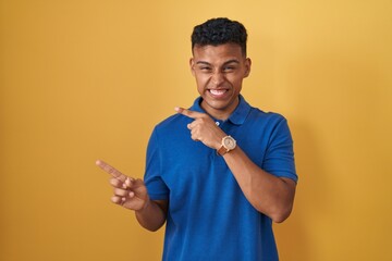 Young hispanic man standing over yellow background pointing aside worried and nervous with both...