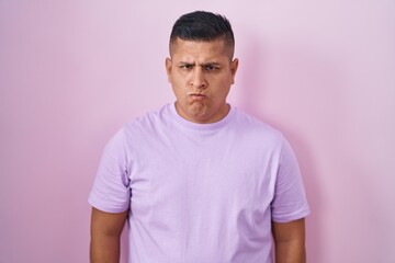 Young hispanic man standing over pink background skeptic and nervous, frowning upset because of problem. negative person.