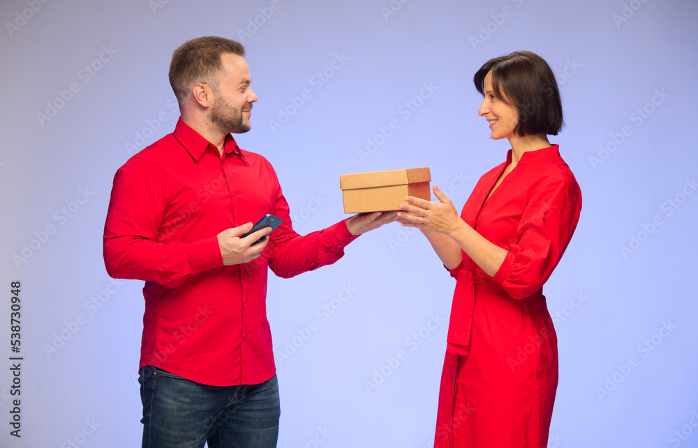 Wall mural joyful smiling couple man and woman with gift box and smartphone tablet in red clothes on blue background isolated.online shopping christmas gifts concept.couple use smartphone tablet.