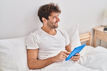 Young man using touchpad sitting on bed at bedroom