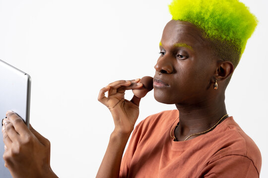 A gay black ethnic man putting on makeup, LGTBI concept, portrait applying blusher with a mirror