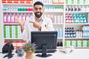 Hispanic man with beard working at pharmacy drugstore amazed and smiling to the camera while...