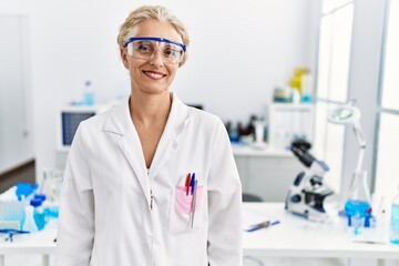 Middle age blonde woman working at scientist laboratory with a happy and cool smile on face. lucky...