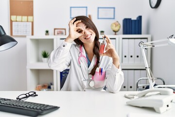 Young doctor woman holding electronic cigarette at medical clinic smiling happy doing ok sign with hand on eye looking through fingers