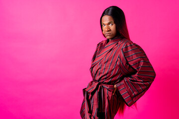 Black ethnic man in a studio, LGTBI concept, with a wig on a pink background