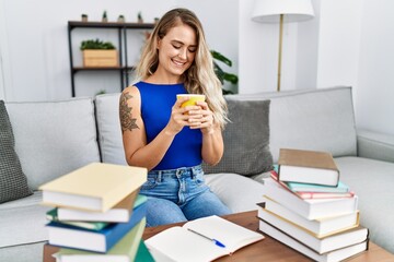 Young woman sitting on sofa studying and drinking coffee at home