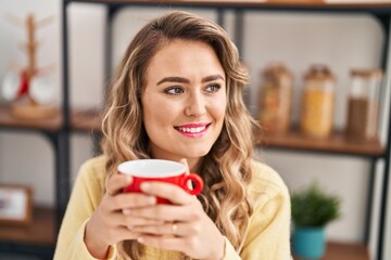 Young woman drinking coffee sitting on table at home