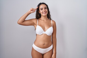 Fototapeta premium Young hispanic woman wearing white lingerie smiling pointing to head with one finger, great idea or thought, good memory