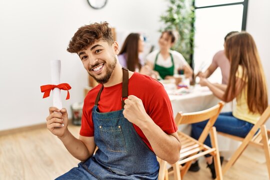 Group of people drawing sitting on the table. Young man smiling happy holding diploma at art studio.