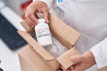 Young hispanic man pharmacist holding package with pills bottle at pharmacy