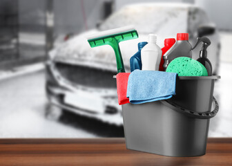 Bucket with cleaning supplies on wooden surface at car wash. Space for text