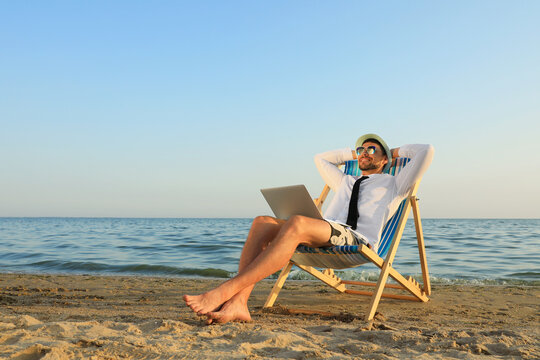 Happy man with laptop resting on deckchair near sea. Business trip - Powered by Adobe