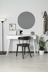 Stylish room interior with round mirror on white wall over desk