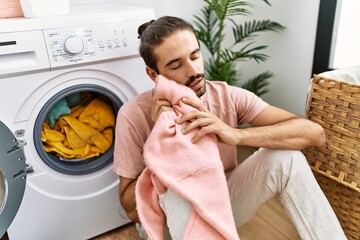 Handsome hispanic man touching soft and fresh laundry at laundry room