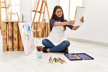 Young latin woman with doubt expression looking notebook draw at art studio