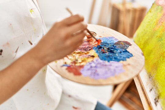 Young latin woman mixing color on palette at art studio