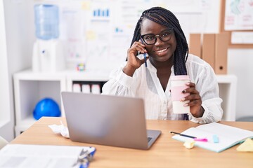 African american woman business worker talking on smartphone drinking coffee at office