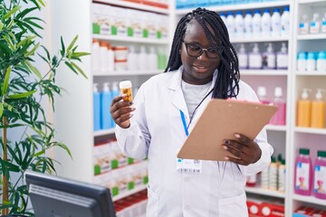 African american woman pharmacist holding pills bottle reading document at pharmacy