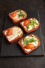 Red beet bread sandwiches with cream cheese, tomatoes and microgreen on black. side view.