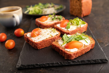 Red beet bread sandwiches with cream cheese, tomatoes and microgreen on black. side view, selective focus.