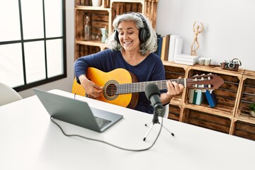 Middle age grey-haired woman playing guitar working at radio studio.