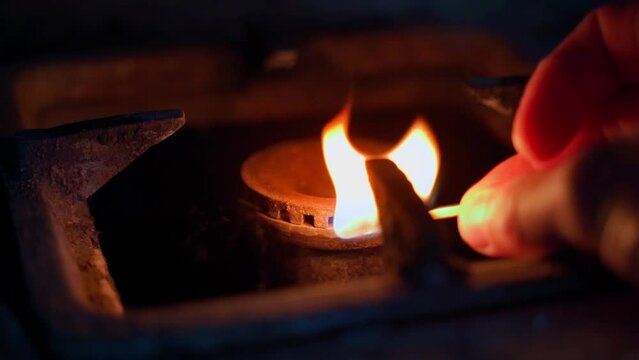 Ignition of gas in the burner with a match. Poor quality gas does not ignite well close-up. A hand with a match is brought in the kitchen stove in the dark. The remains of blue fuel in the pipes.