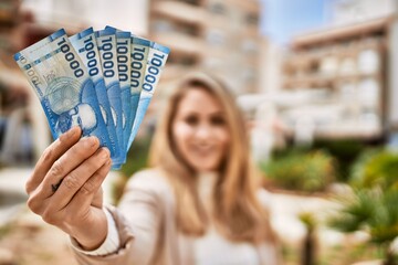 Young blonde woman smiling confident holding chilean pesos banknotes at street