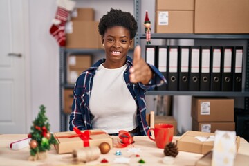 Fototapeta premium African american woman working at small business doing christmas decoration smiling friendly offering handshake as greeting and welcoming. successful business.