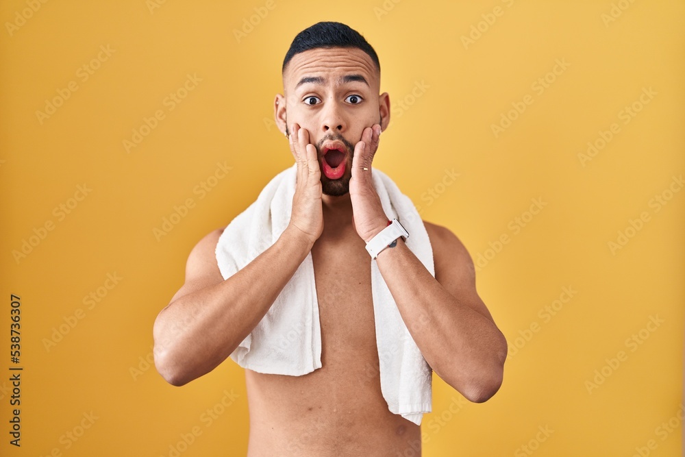 Poster young hispanic man standing shirtless with towel afraid and shocked, surprise and amazed expression 