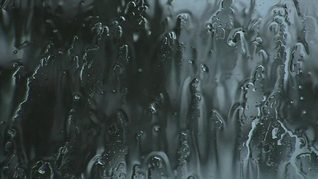 Raindrops fall on a window pane.