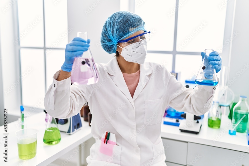 Wall mural young latin woman wearing scientist uniform holding test tubes at laboratory