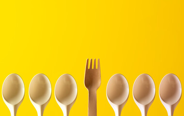 wooden fork and plastic spoons on yellow background
