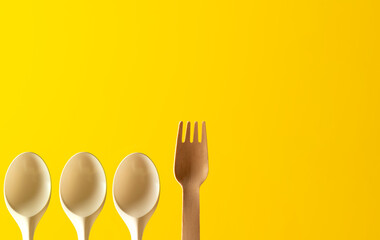 sustainable fork among plastic spoons on yellow background
