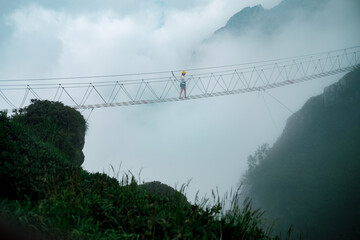 Woman on a footbridge between two mountains at the middle of this risky walk with the beautiful view