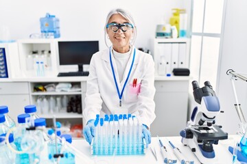 Middle age grey-haired woman wearing scientist uniform looking positive and happy standing and smiling with a confident smile showing teeth