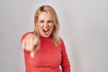 Blonde woman standing over isolated background pointing displeased and frustrated to the camera,...