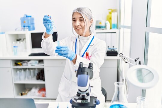 Middle age grey-haired woman wearing scientist uniform using pipette at laboratory