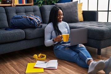 African american woman student using laptop drinking coffee at street