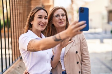 Mother and daughter making selfie by the smartphone standing together at street