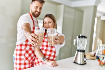 Young couple smiling confident holding glass of smoothie at kitchen