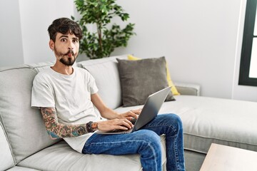 Hispanic man with beard sitting on the sofa making fish face with lips, crazy and comical gesture. funny expression.