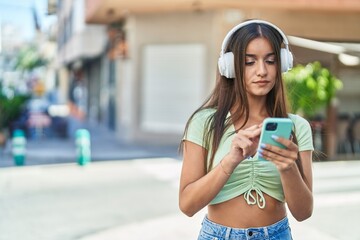 Fototapeta premium Young beautiful hispanic woman listening to music at street
