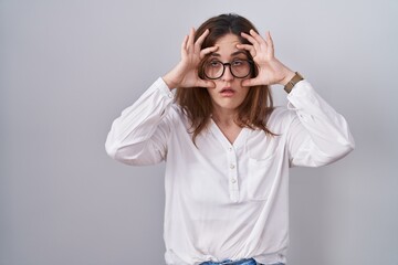 Brunette woman standing over white isolated background trying to open eyes with fingers, sleepy and tired for morning fatigue